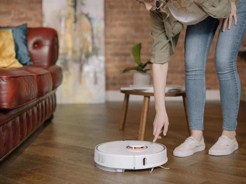 Woman using a robot vacuum to clean the living room floor.
